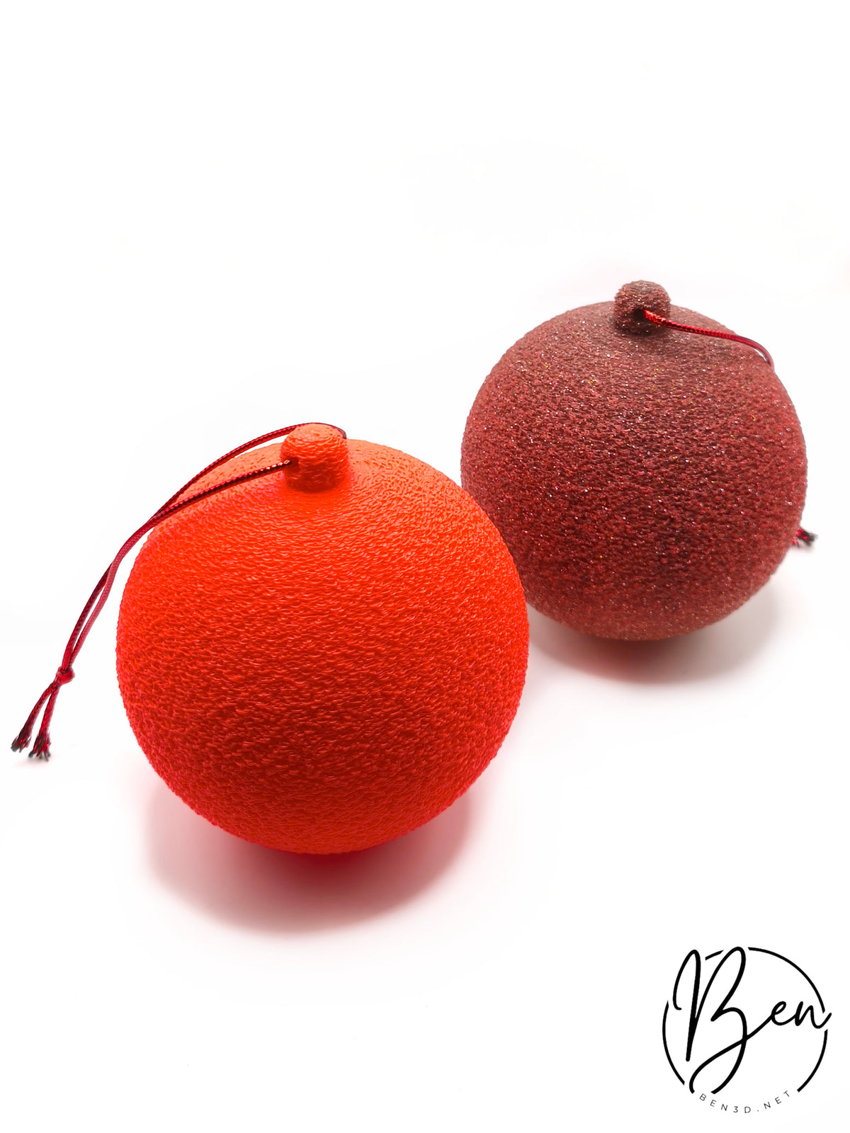Dos bolas de Navidad con superficie texturizada en naranja y rojo oscuro, con cordones para colgar